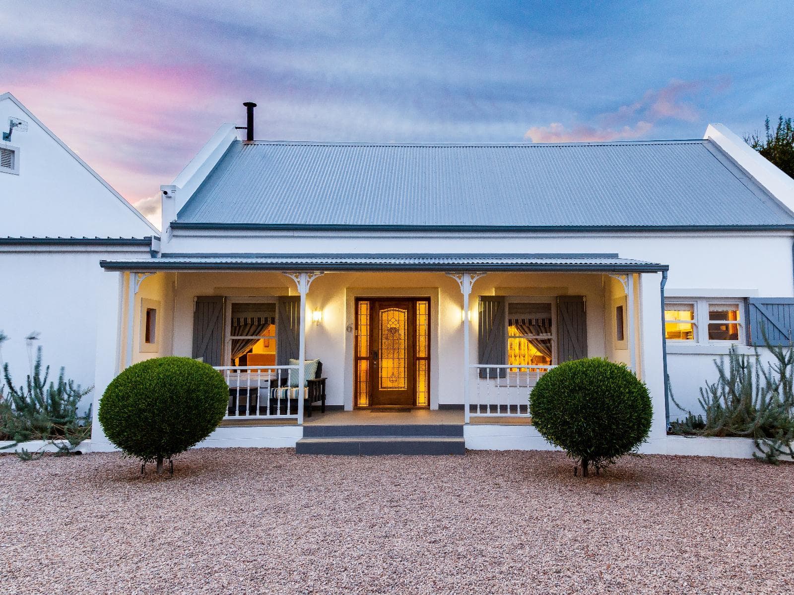 Karoo View Masterclass: White Karoo cottage with lit porch under pink sunset sky