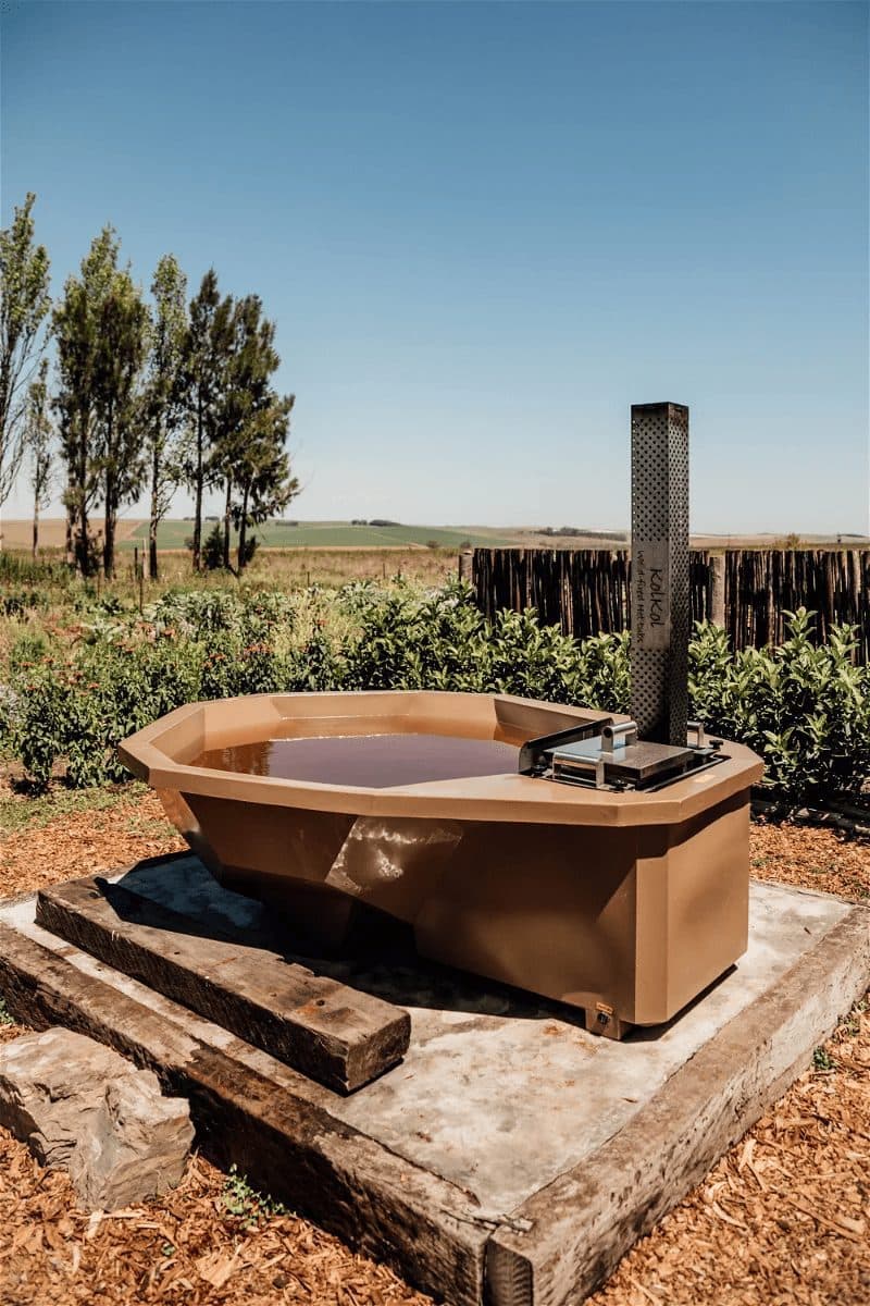 Choctaw Cottage at Bokrivier: Wood-fired hot tub with chimney heater on open farmland under blue sky