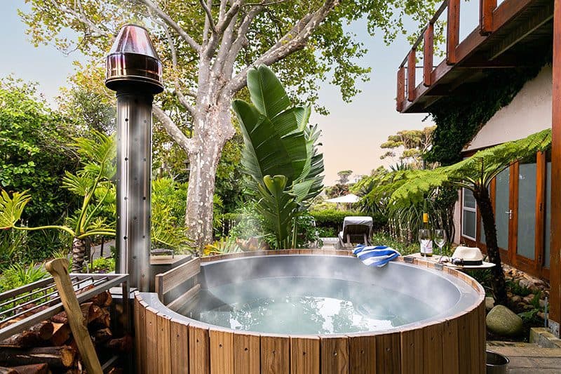 Camps Bay Retreat: Steaming wooden hot tub at dusk in lush garden, wine and towel