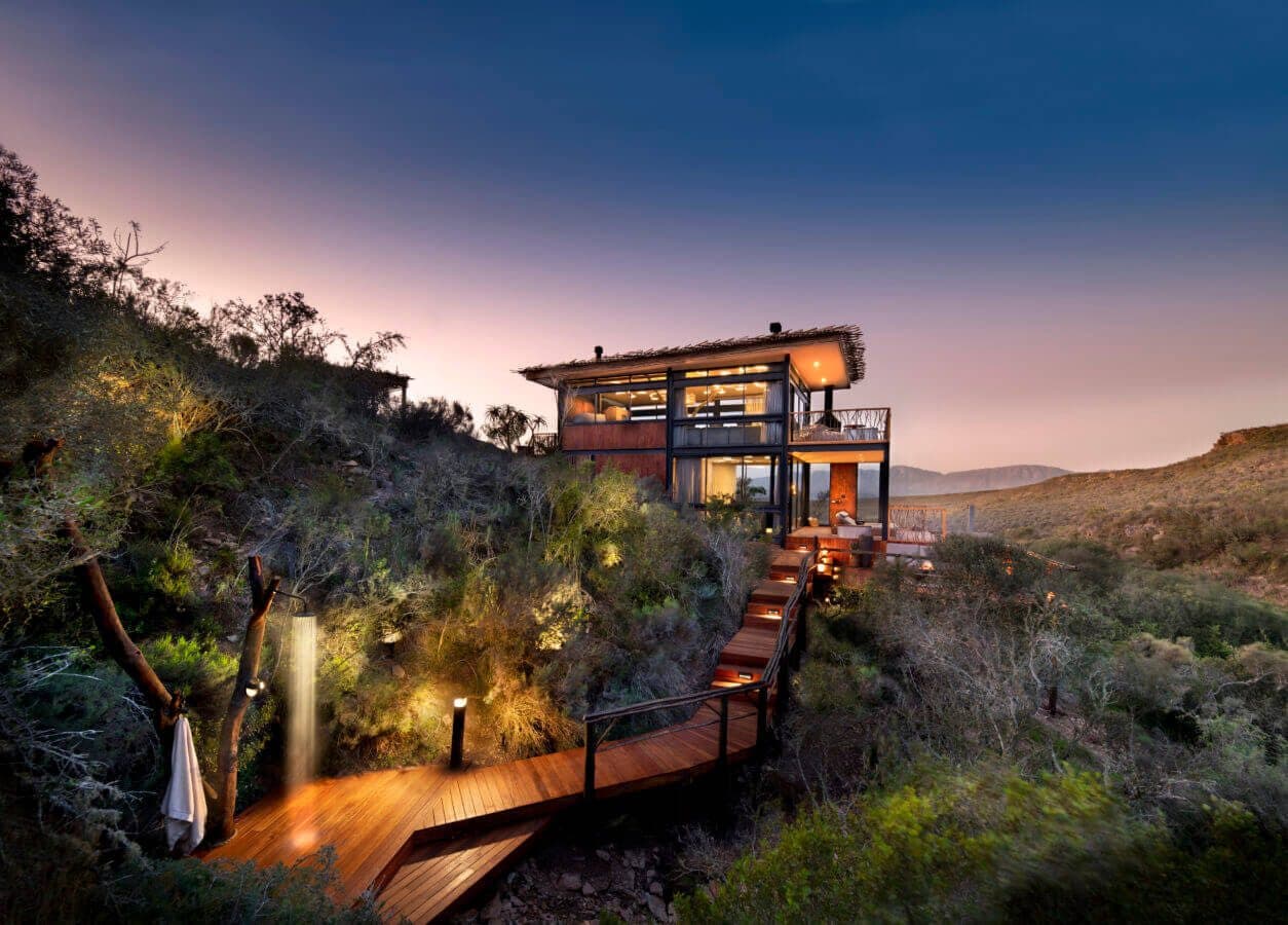 Melozhori Treehouse: Lit treehouse cabin at dusk on hillside, boardwalk and shower