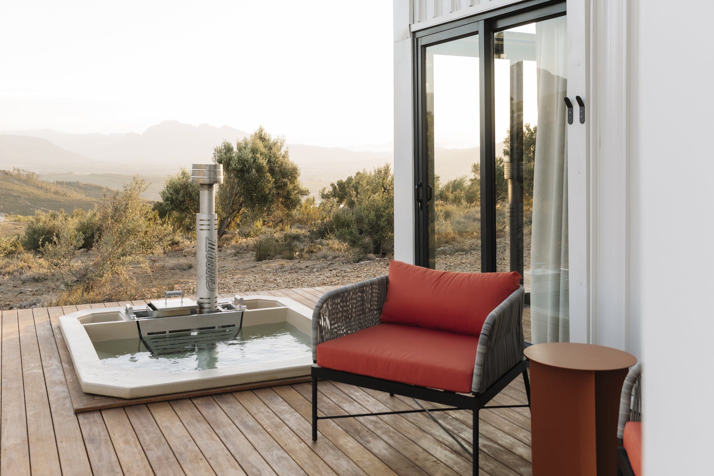 Hemingway Untether Luxury Pod: the sunken wood-fired hot tub on the deck at golden hour, looking over the Winelands valley