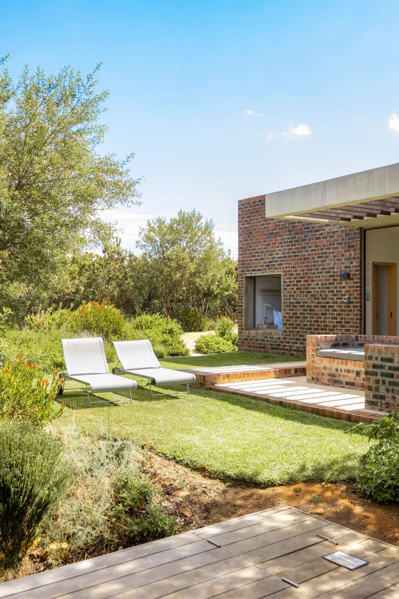Earth Eco Cabin at Stonehaven: Sun loungers on green lawn beside brick cabin, bushveld behind
